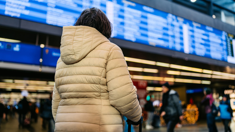 Backside view of a traveler with a puffy coat looking at the departures board