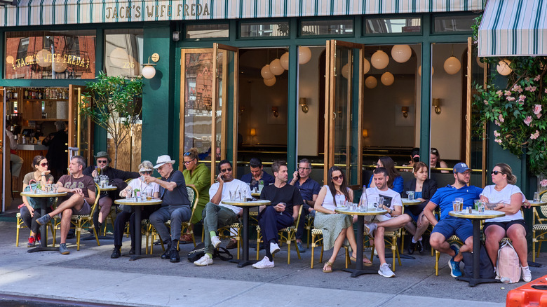 Outdoor diners at tables facing a sidewalk at a restaurant in New York City