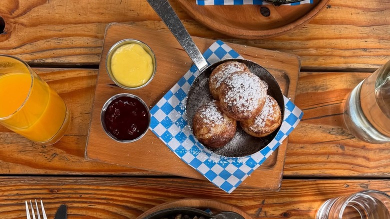 A plate of Danish pancakes coated in powdered sugar, served with lemon curd and lingonberry jam