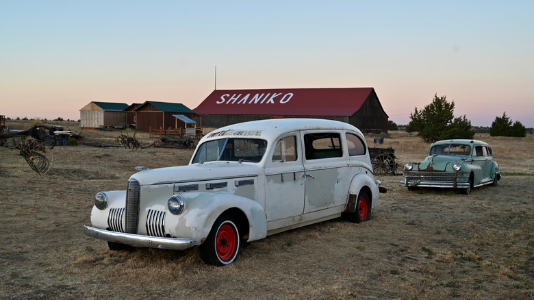 Old cars in Shaniko, Oregon, with red-roofed building in the background.
