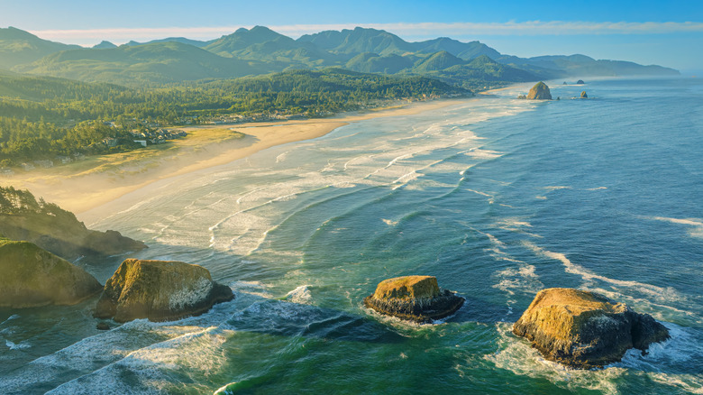 Rrugged Oregon coastline with waves crashing on scenic rocks and lush green mountains in the background