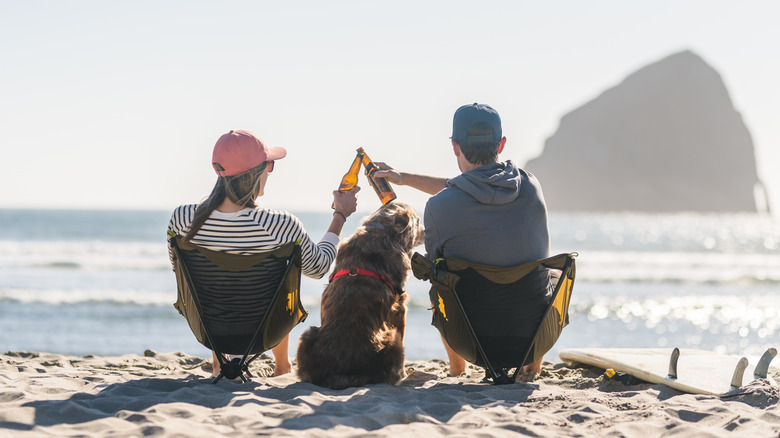 Two people toast their beers on the beach overlooking Haystack Rock, Pacific City, Oregon