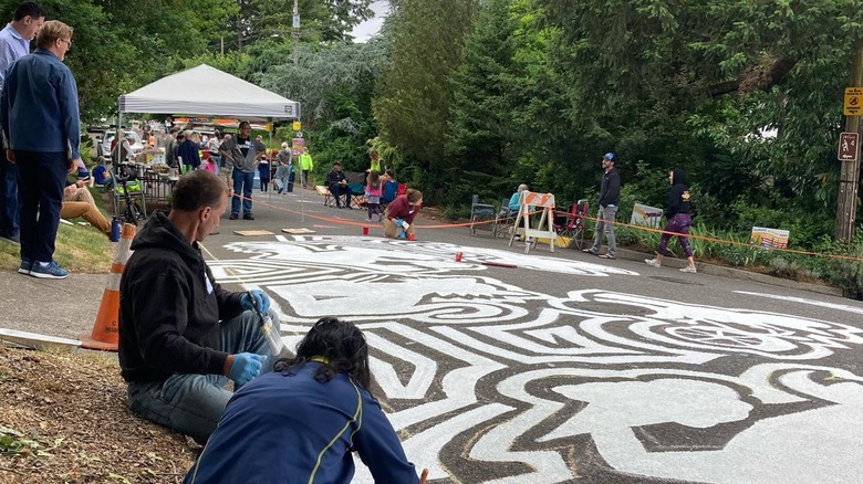 People work on a sidewalk mural in Multnomah Village, Portland