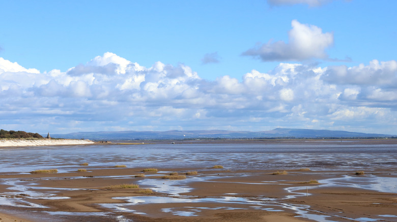 A view across the Ribble estuary featuring sandy dunes, water, and a cloudy sky