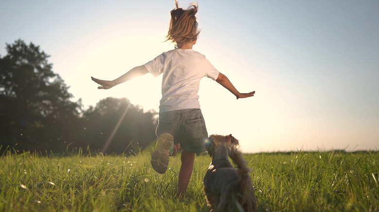 A young girl and her dog dash across the park grass