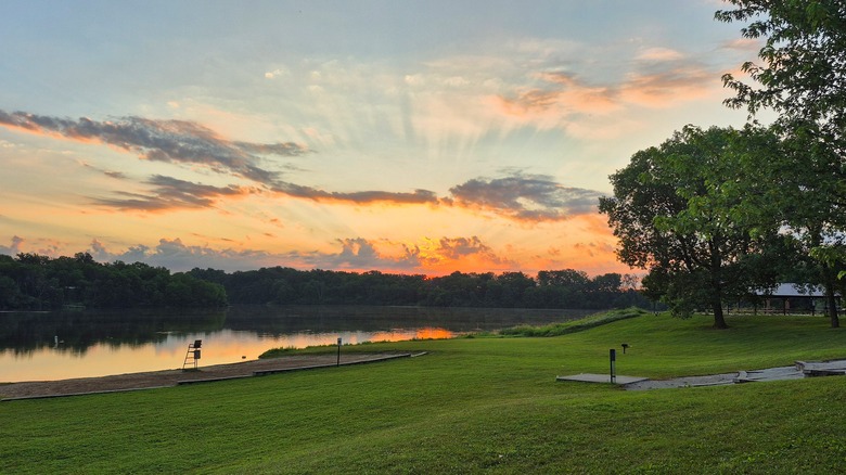 A green manicured lawn area next a small beach next to a lake at the Briggs Woods park at sunset