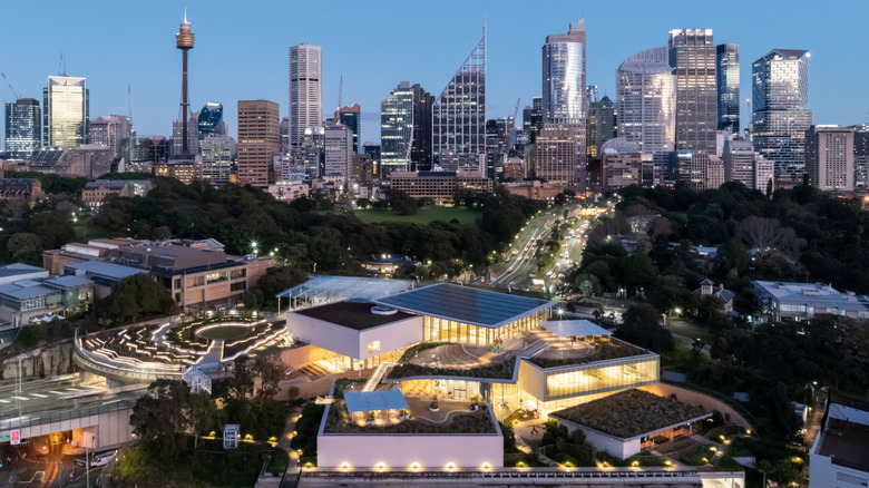 Aerial view of the Art Gallery of New South Wales' Naala Badu building looking towards the Domain and the city at dusk, featuring Jonathan Jones' art commission 'bíal gwiyúŋo (the fire is not yet lighted)' in the final stages of construction, 2024