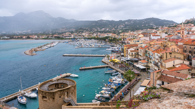 The harbor in Calvi, Corsica, France with colorful buildings, boats, and mountainous backdrop