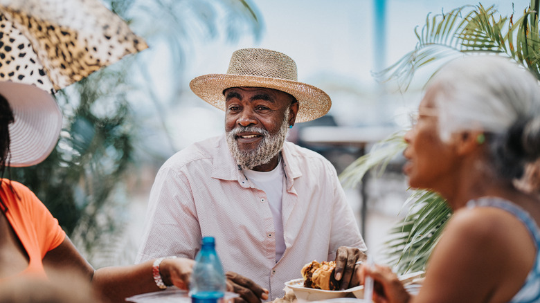 Three relaxed retirees laugh and share food around a table.