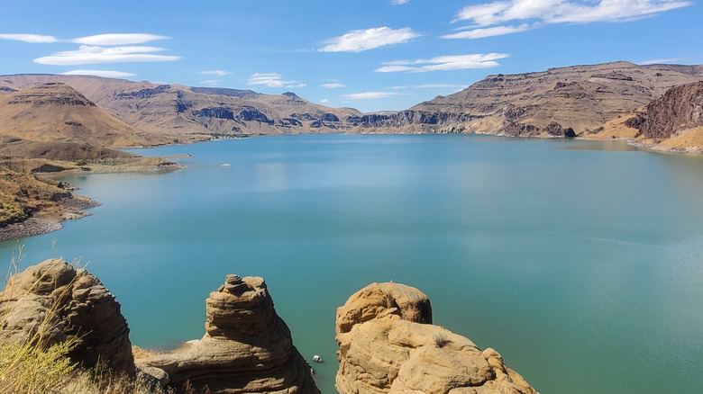 An aerial view of a blue lake in the desert, surrounded by cliffs and rocks
