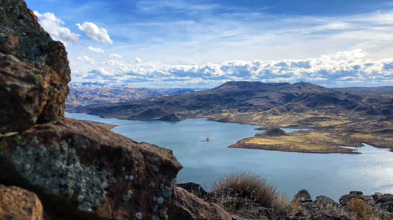Aerial view of a lake with a boat in the middle, surrounding by rocky hills and mountains