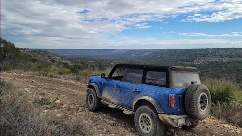 A mud-spattered blue vehicle driving up an off-road track in Escondido Draw Recreation Area in Ozona, Texas