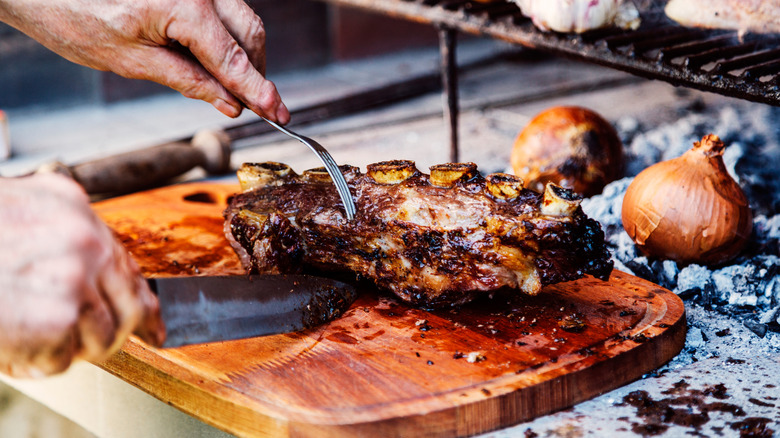 Asado beef meat being sliced on a wooden cutting board