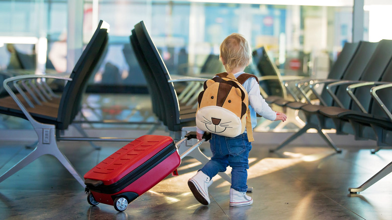 Child at airport with luggage and a lion backpack.