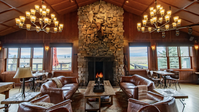 Interior of a rustic lounge area with chandeliers, couches, and a burning fireplace at Paws Up Montana