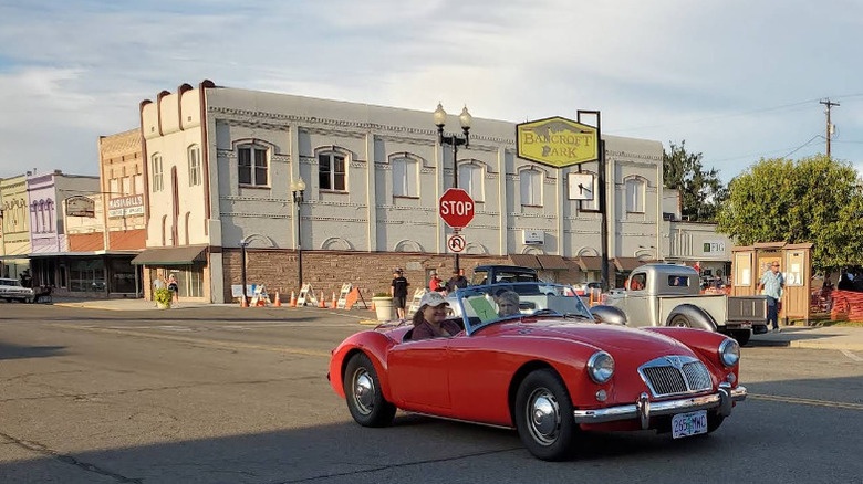 Two people in a classic red car in front of a historic building in downtown Payette, Idaho.
