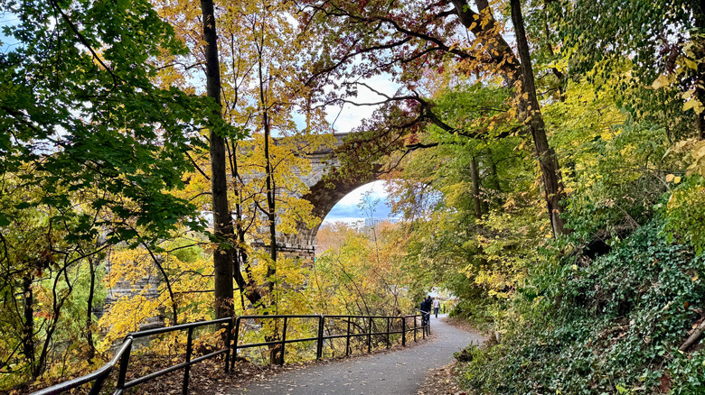 Man walking on the Wissahickon Bike Trail along the creek with the viaduct bridge in the background in Wissahickon Valley Park, Philadelphia, Pennsylvania