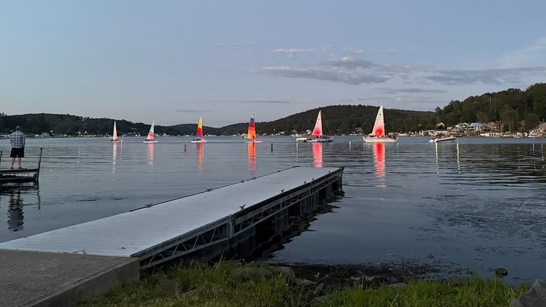 Colorful sailboats on Harvey Lake under a blue sky, with a dock in the foreground and trees on the far shore
