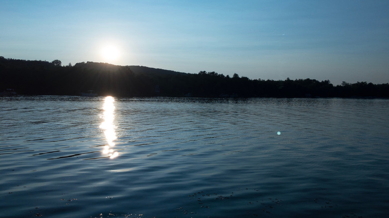 Canadohta Lake at sunset, with shadowy trees between a blue sky and water