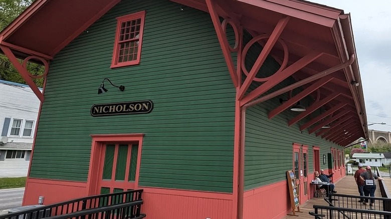 Nicholson Tourism Center, a green-walled building with maroon accents and people on the front porch, with the Tunkhannock Viaduct in the background