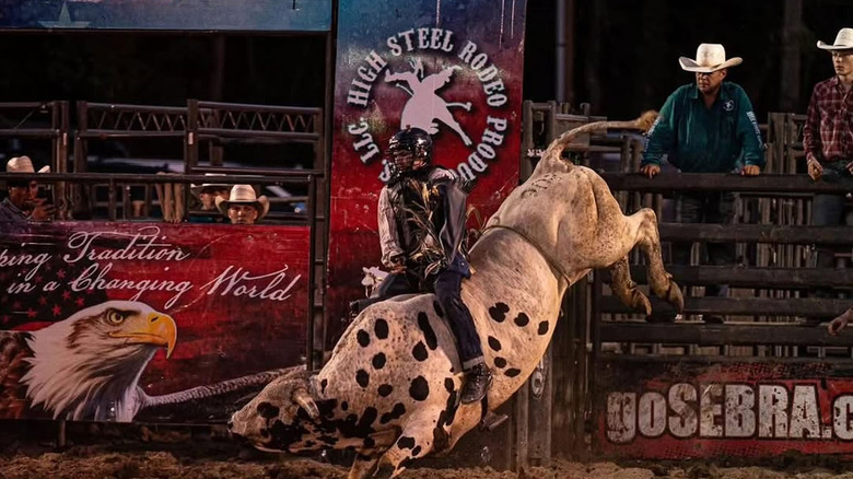 Person in a helmet riding a black-spotted white bull at the Little A Town Rodeo