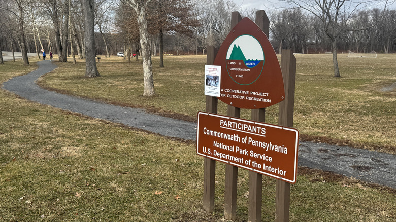 A sign for Milton State Park in Pennsylvania with a trail in the background