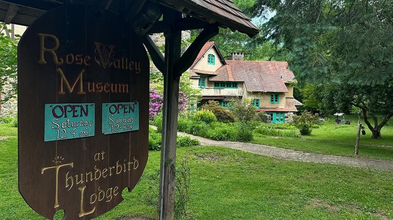 Rose Valley Museum sign in the foreground with trees surrounding a yellow building with green windows in the background