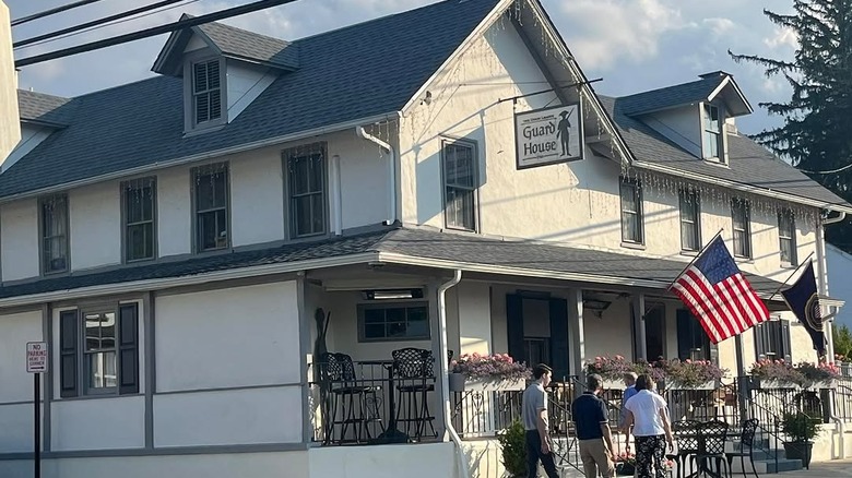 The Union League Guard House in Gladwyne, a white building with a black roof and an American flag out front under a cloudy sky