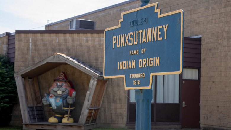 Sign for Punxsutawney with its date of founding, with the firehouse and a groundhog statue in the background