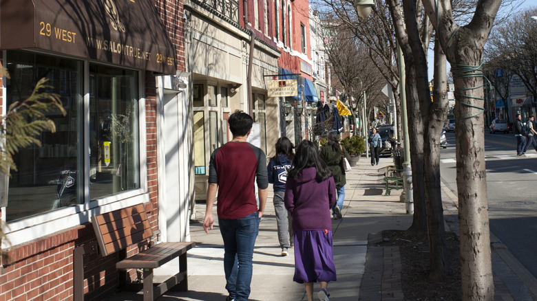 People walking down a sidewalk in a Philadelphia suburb, with stores along the left of the frame and a street along the right