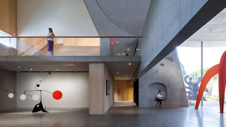Visitors view red and black sculptures in the concrete indoor portion of Calder Gardens