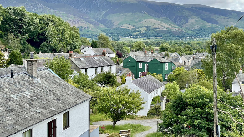 View of a green building amid whitewashed homes against green hills in Braithwaite, Lake District