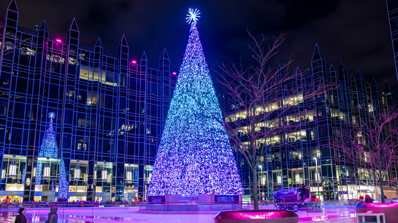 Zamboni cleaning an outdoor rink around a Christmas tree covered in white lights at night, with the PPG building in the background