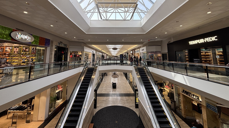 Interior of Ross Park Mall, with white hallways and parallel escalators between two-story walls lined in storefronts under a skylight