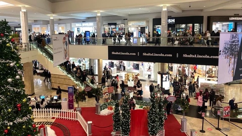 Interior of Ross Park Mall at Christmas time, with crowds walking on both levels of a two-story white-walled mall, with a red carpet and Christmas trees in the foreground