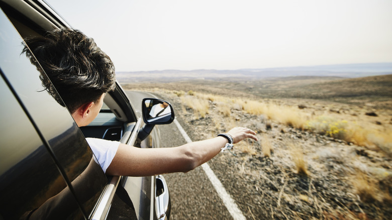 A man with his hand out of the car during a road trip