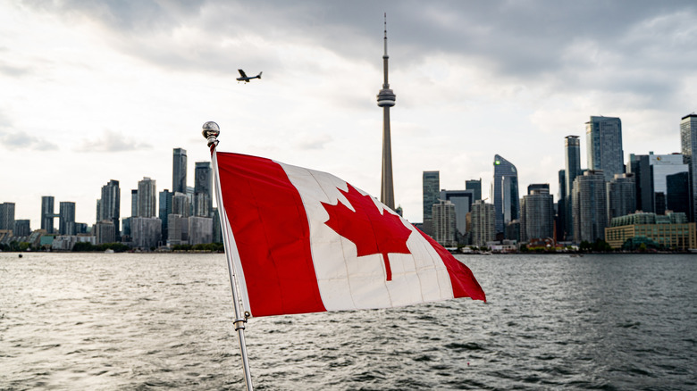 Canadian flag flying in front of water with cityscape of Toronto in the background