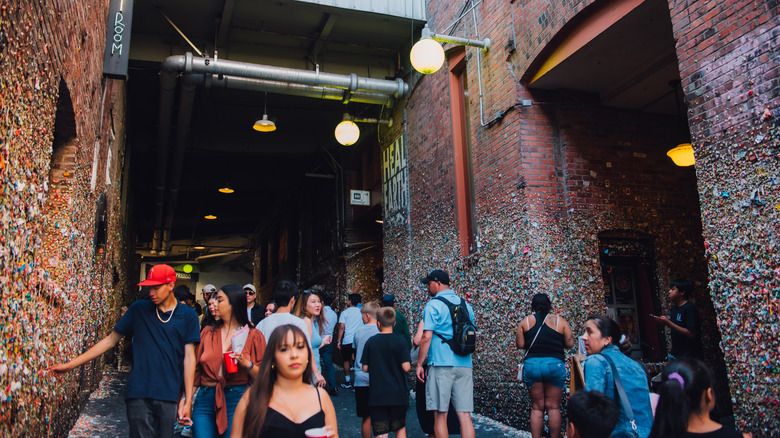 People walking through Post Alley underneath Pike Place Market with chewing gum covering the lower portion of the brick walls.