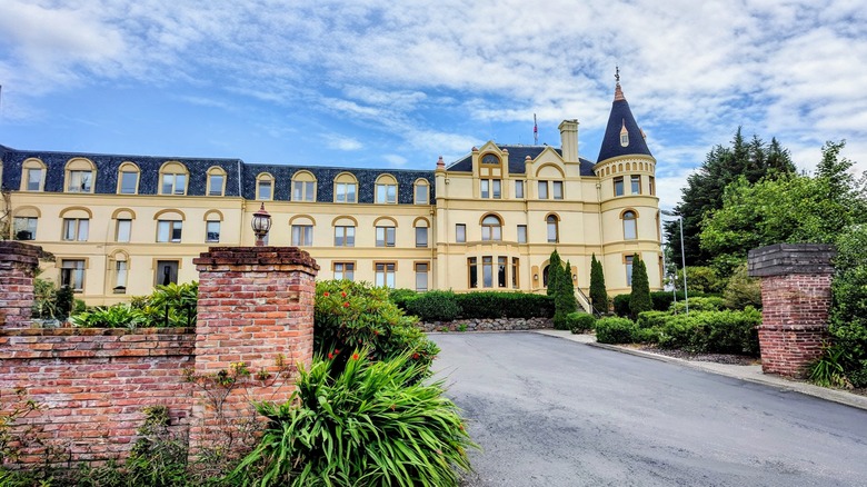 Manresa Castle Hotel, an elegant historical building with a tower, arched windows, and manicured landscaping, surrounded by a brick wall and greenery on a sunny day in Port Townsend, Washington.