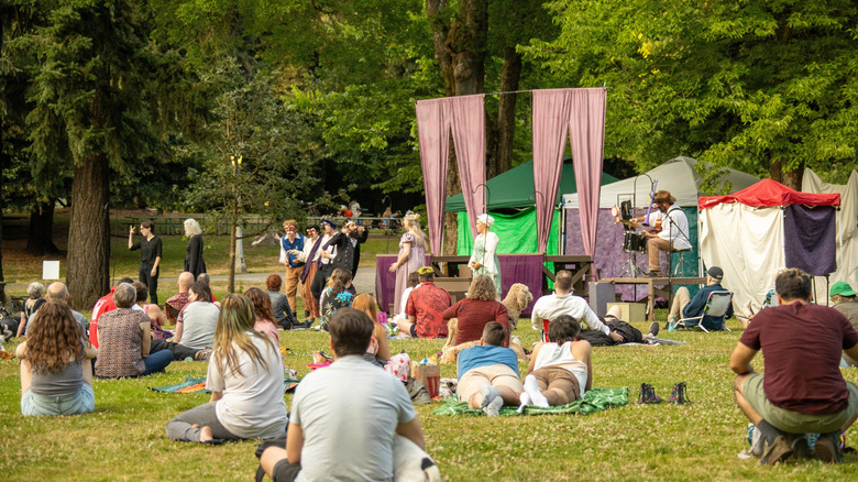 Crowd in Laurelhurst Park watches a Shakespeare troupe performing, surrounded by trees