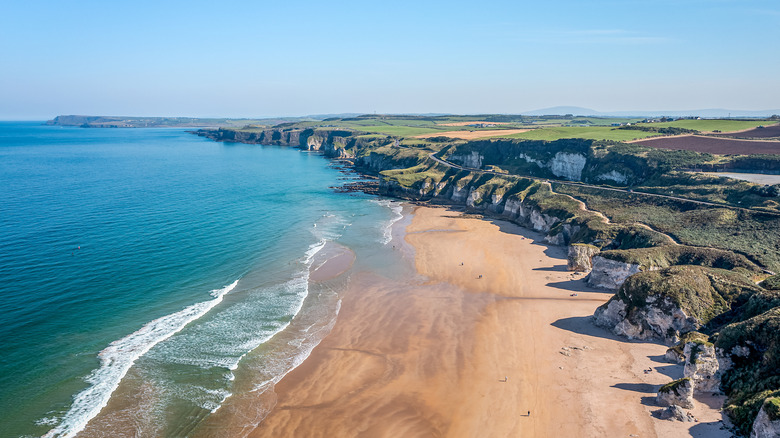 White cliffs topped with grass overlook the white sand and sea at Whiterocks Beach in Portrush, Northern Ireland
