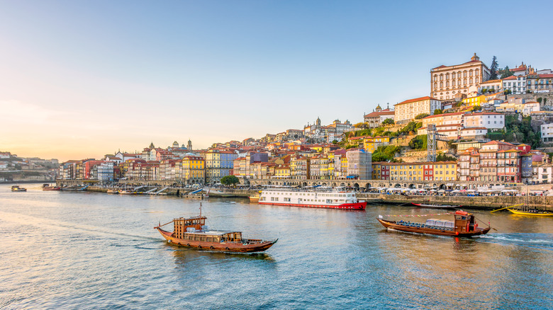 A view of Porto, Portugal, a city on the water at golden hour with several boats in the foreground