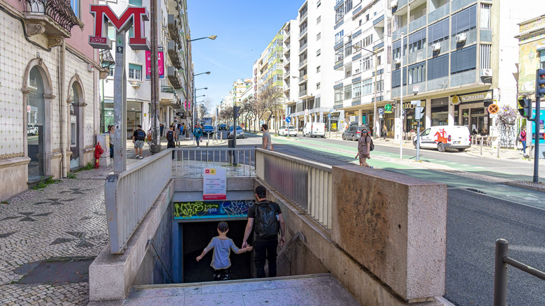 A man and boy walking into the Anjos metro station with shops and apartments nearby.