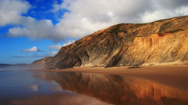 Cliffs reflected on the wet sand of a deserted beach in Alentejo Natural Park