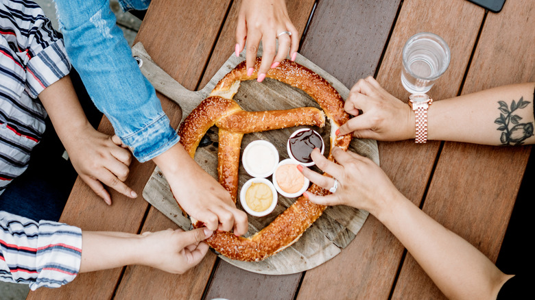 Overhead angle of arms and hands grabbing a soft pretzel on a table
