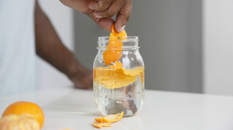 Hand placing tangerine peels into glass jar