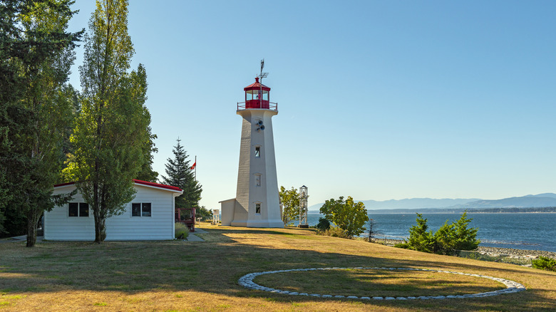 Historic lighthouse on Quadra Island in British Columbia with pebble beach and water in foreground