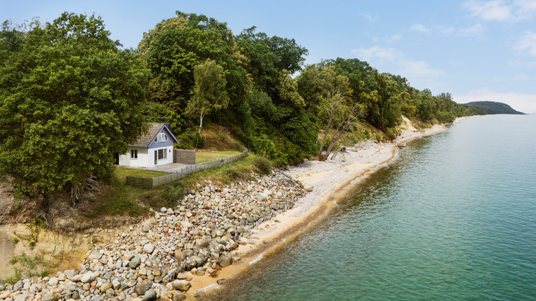 A cabin overlooks a rocky beach and placid water in rural Sweden on a beautiful summer day