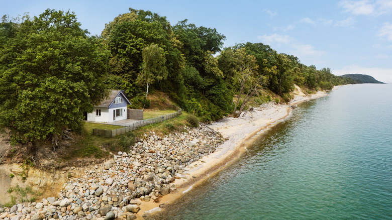 A cabin overlooks a rocky beach and placid water in rural Sweden on a beautiful summer day