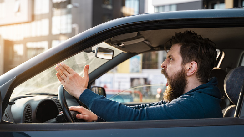 a man angrily yells from inside his car with the window rolled down